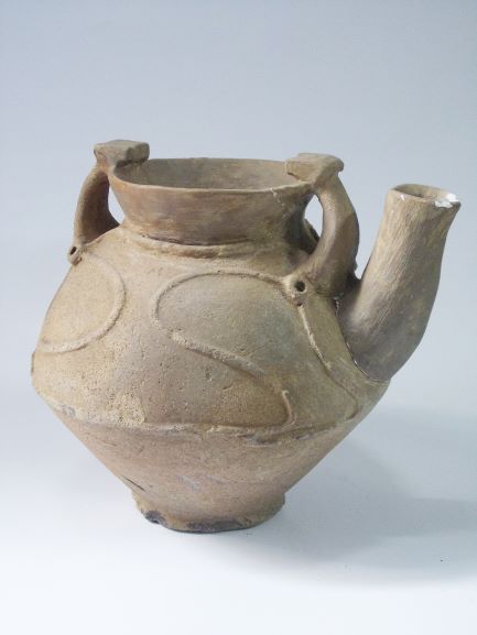 胴体部分には円や曲線で構成された文様が施され、口縁部に2つの把手があり、上向きの注ぎ口がある注口土器の写真