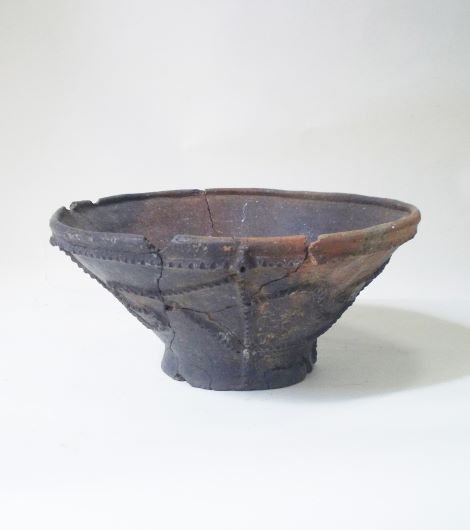 上部が大きく開き、底部が小さくすぼまった鉢形で、胴部には縄目や点描で構成された複雑な文様が施されており、表面は黒く変色した土器の写真