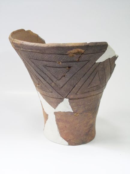 口縁部が大きく広がり、胴体上部には複数の三角文様と縄目文様が施され、破損した箇所を白い補修材で補修した深鉢形土器の写真