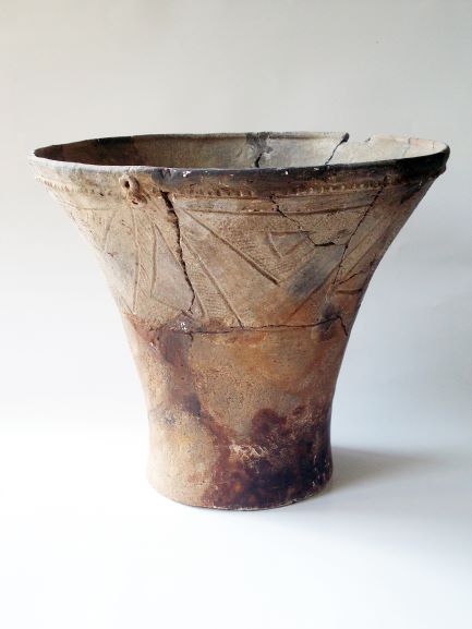 口縁部から底部にかけて広がった深鉢形で、胴部には複数の三角形の文様が施され、ひび割れや変色が見られる土器の写真