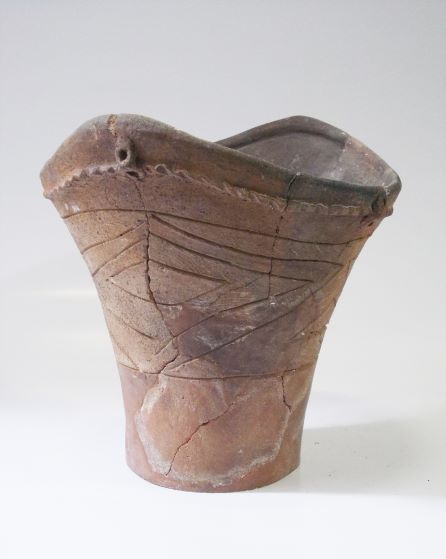 口縁部が波打った形状で、胴体上部には横線と斜めの線で構成された文様が施され、全体的にひび割れや変色が見られる土器の写真