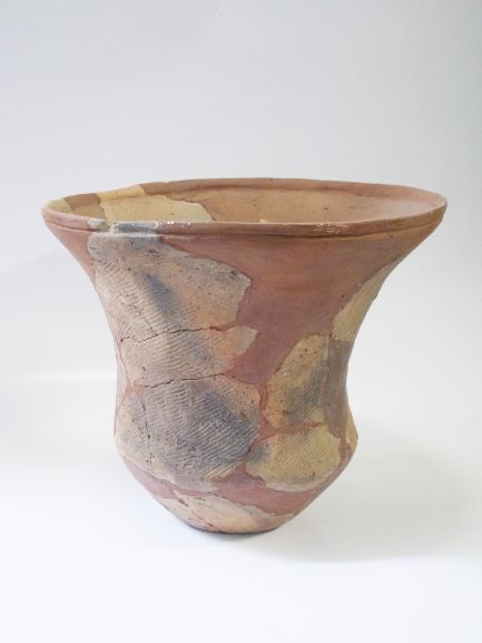 口縁部から底部にかけて広がった形状で、胴部には縄目文様見られ、茶色の修復跡で補修された土器の写真