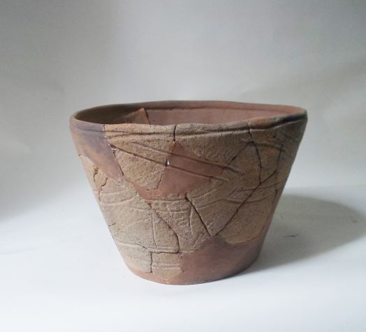 口縁部から底部にかけて広がった深鉢形で、胴部には複数の三角形や斜めの線で構成された文様が施され、ひび割れや変色が見られる土器の写真