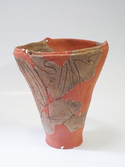 口が開いた底部に向かってすぼまった深鉢形の、胴体には縄目と曲線で構成された文様が施され、破損した箇所が茶色の修復材で修復された土器の写真