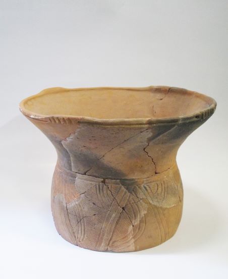 口縁部が大きくラッパ状に広がり、胴部には縄目文様が施され、ひび割れや変色が見られる土器の写真