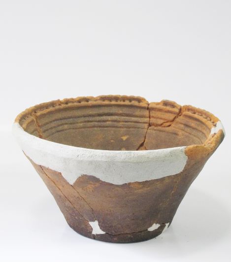 一部が欠損し白い修復材で修復がされた鉢形で内側に複数の平行な線の模様施された土器の写真