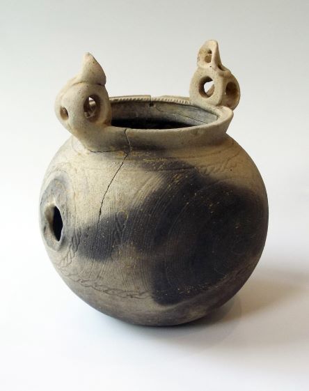 球体に近い形状で、胴体に小さな丸い開口部が1つ見られ、上部には左右に2つの突起がある注口土器の写真