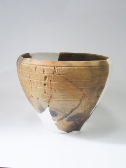 線状の模様が刻まれた、欠損部が白い修復材で復元されている鉢形土器の写真