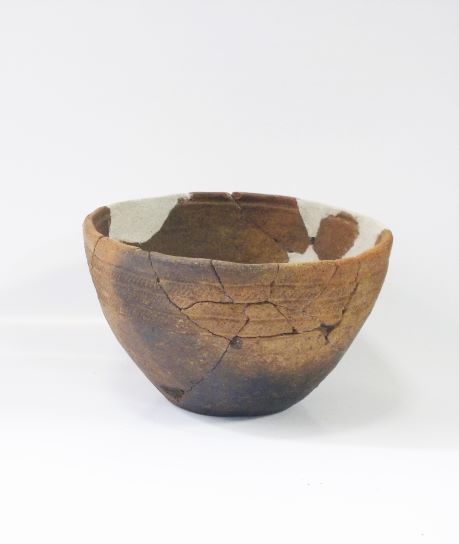 縁の部分が白く補修されており、線で模様が入った鉢形土器の写真