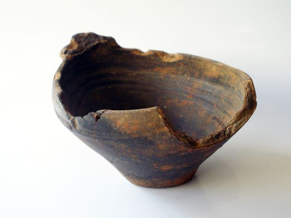 縁の大部分が大きく欠け、ひび割れが見られる、表面が黒く変色した土器で、内側には同心円状の模様がある浅鉢形土器の写真