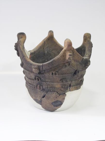 複雑な文様と複数の突起の装飾が施された、縁が王冠のように波打つ深鉢形の土器の写真