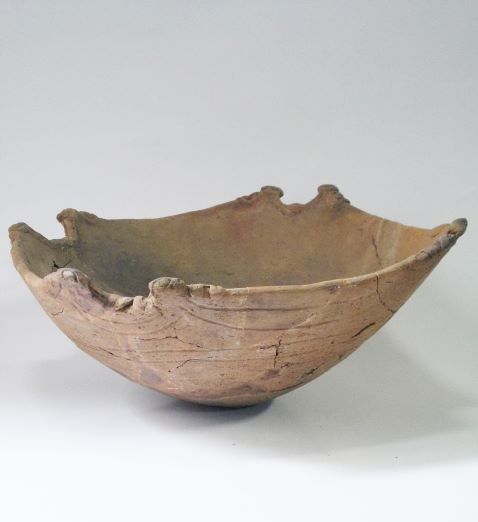 縁の数箇所が波打つように盛り上がり、胴体には横方向の線状の文様が見られる浅鉢形土器の写真