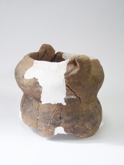 数箇所が白い補修材で修復された、口の部分が波打つように盛り上がり、丸みを帯びて、くびれがある土器の写真