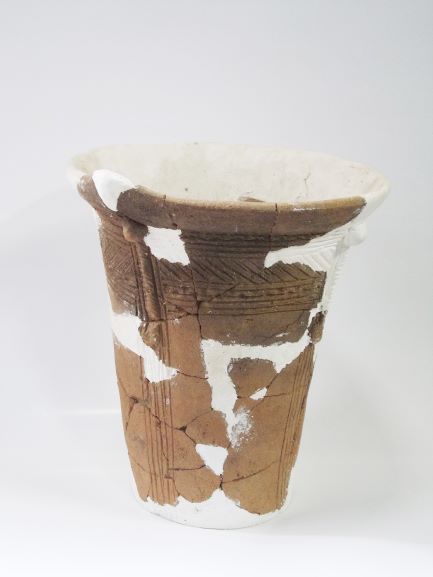 白い補修材で繋ぎ合わせられた薄茶色の深鉢形で、上部と下部にそれぞれ模様が施されている土器の写真