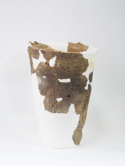 白い補修材でつなぎ合わされた、薄茶色の深鉢形で、表面に縦横に引かれた線のような文様が刻まれている土器の写真