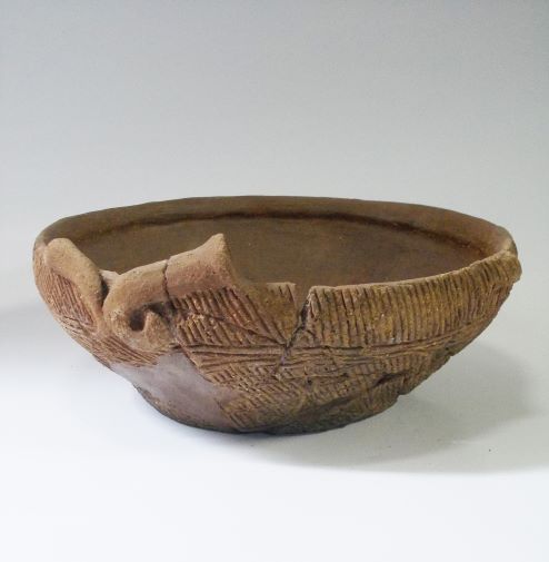 いくつかの破片をつなぎ合わせて修復された浅鉢形で、表面に複数の文様が複雑に施されている土器の写真