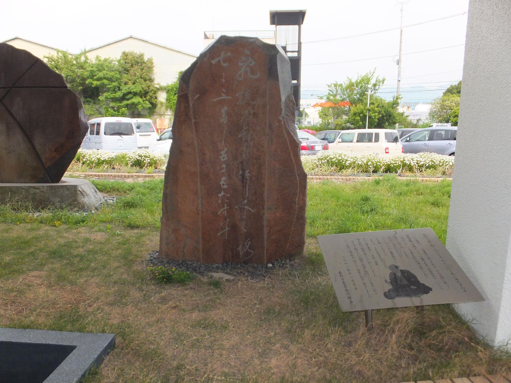 駐車場の前にある芝生の広場に茶色の石碑と案内板が建っている写真