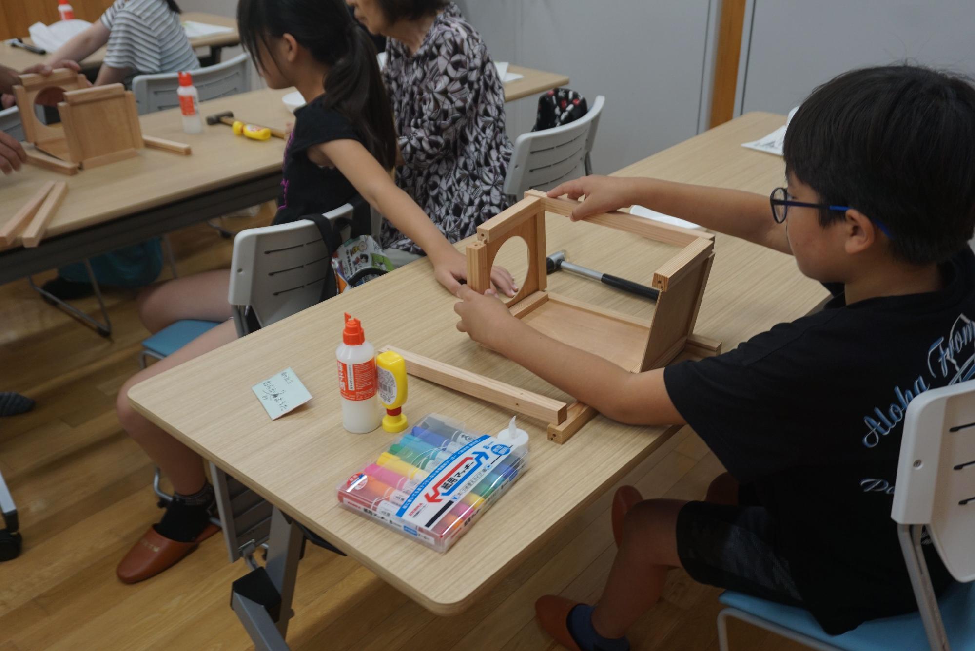 ボンドやカラーペンが置かれたテーブルに向かい、あんどんの木枠を組み立てている参加者たちを後方から写した写真