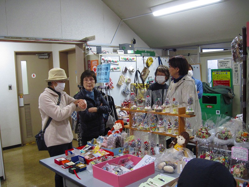 クリスマスのクラフト作品や、人形、装飾品などの様々な小物を展示・販売しているブースを囲んで女性が話をしている写真