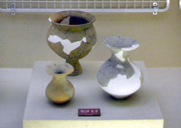 白く修復された部分が目立つ、破損した3つの古い土器が展示台に並んで置かれている写真