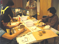 複数の参加者がテーブルを囲み、土をこねたり形を整えたりして土器づくりに取り組んでいる様子の写真