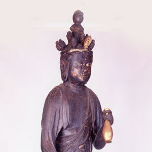 黒く古びた仏像の上半身の胸から上を写し、宝冠を被り左手に金色の水瓶を持った木造十一面観音菩薩坐像の写真