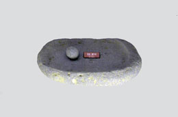 楕円形の石皿とその上に置かれた丸い磨石が展示されている縄文時代の石器の写真