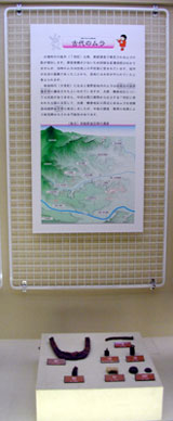 歴史資料館に展示された、説明文と地図が記載されたポスター、その下にガラスケースに入った出土品を写した写真