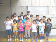 参加者の子どもたちが、屋外の白い壁の前で拳を握ってポーズをとり、カメラに向かって立っている集合写真