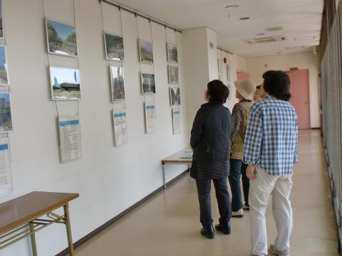 廊下の壁にたくさんのパネルが吊り下げて展示され、その前で複数の女性たちが熱心にパネルを見ている様子の写真