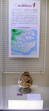 透明なケースの中に展示された土器が置かれ、その上部には関連する地理情報を記した地図と説明文が掲示されている写真