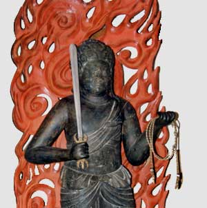 朱色の火炎光背の前に立っている、黒色で右手に剣、左手に羂索を持った木造不動明王立像の写真