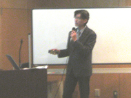 柏木先生がホワイトボードの前でマイクを持って話をしている様子を撮影した写真