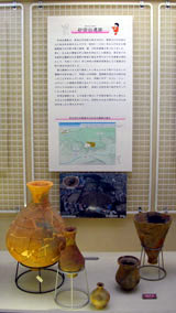 複数の石器が展示台に並べられ、背景の壁には砂田台遺跡に関する説明文と地図や航空写真が掲示されている写真