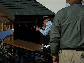 双体道祖神がまつられた祠の前で、男性が深くお辞儀をしながら玉串を奉納しており、その様子を後ろに立った男性が見守っている様子の写真