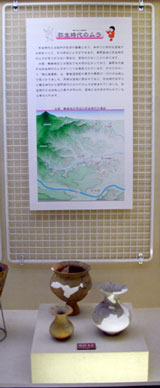 3つの異なる形をした土器が展示台に並び、その上部に周辺の地理情報と説明文が書かれた掲示物が設置されている展示コーナーの写真
