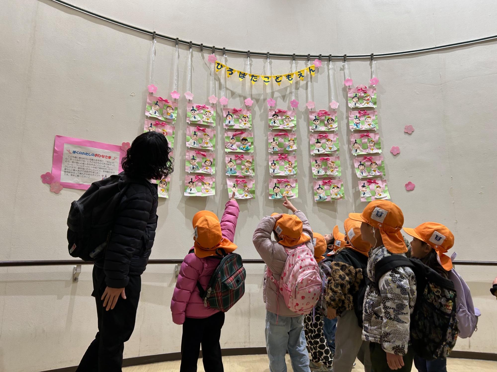 壁に展示しているひな人形を園児数人が見ています。