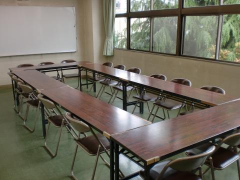 6脚の長机がロの字型に並べられた集会室内の写真