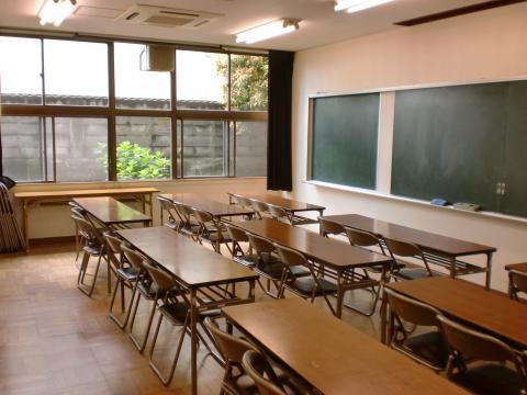 黒板に向かって長机が数脚並べられ、ガラス窓から外光が差し込んでいる学習室の写真