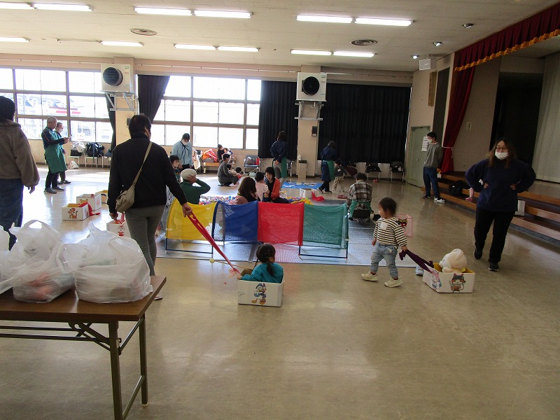ホールの中で幼児数名が大人数名といろいろなおもちゃで遊んでいる