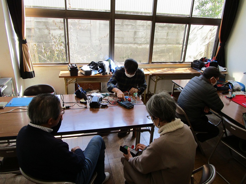 おもちゃを修理しているのを二人の大人が見ている。