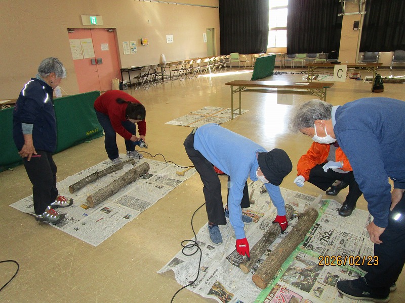 二組の講師と聴講者が原木にシイタケの植菌をしている。