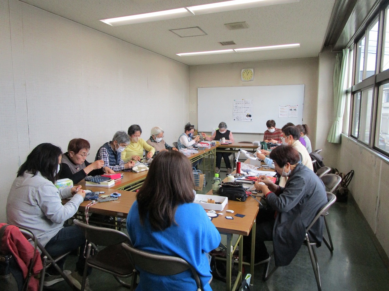 女性十数人が机に着席して縫い物をしている。
