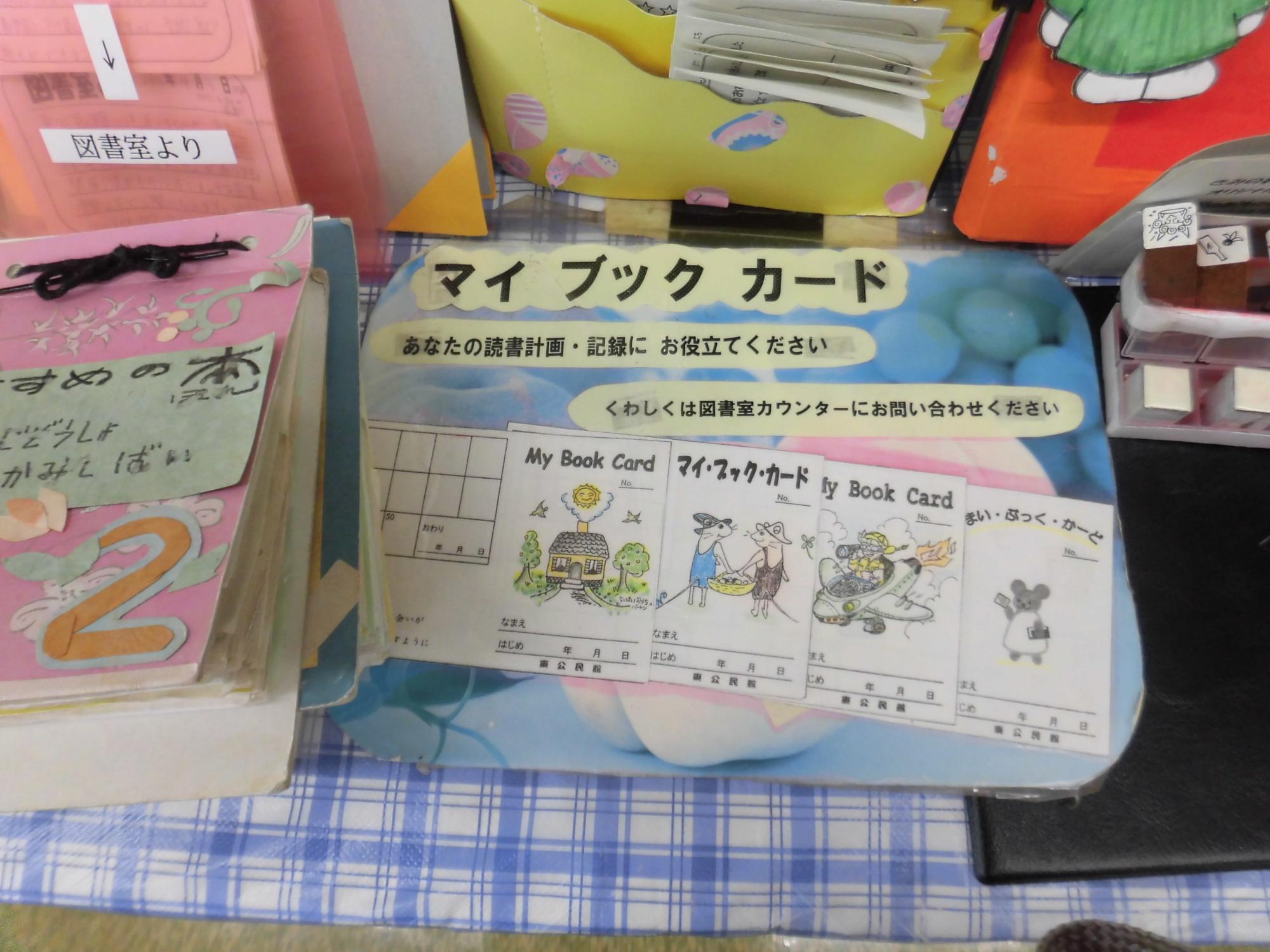 子供たちの読書記録に役立つ「マイブックカード」の見本がテーブルに置かれており、かわいらしいイラストと共に利用方法が記載されている図書室の備品の写真