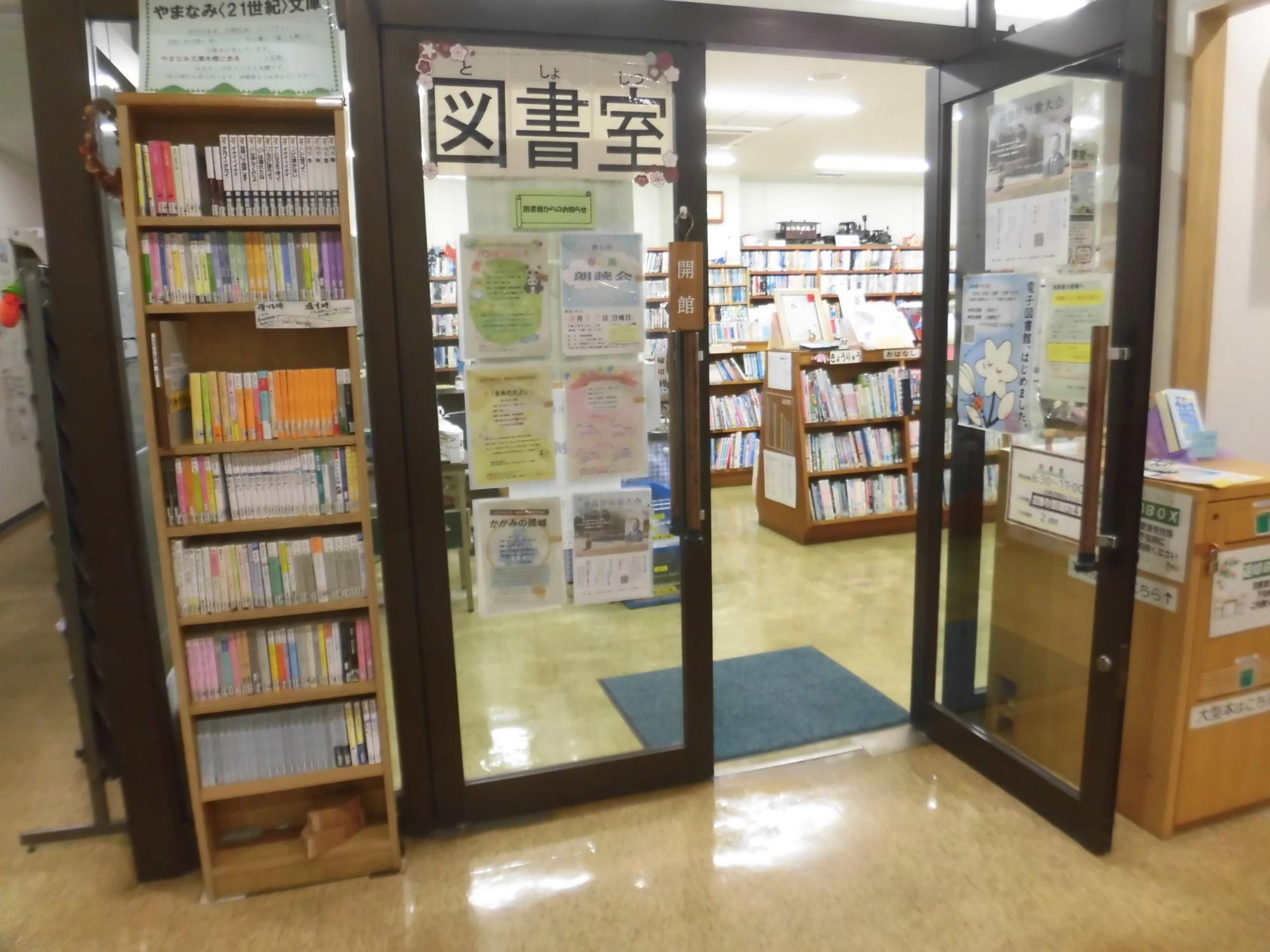 茶色の縁のガラスドアに「図書室」の文字シールが貼られ、奥には本がぎっしりと並んだ棚が複数見える、図書室入口の写真