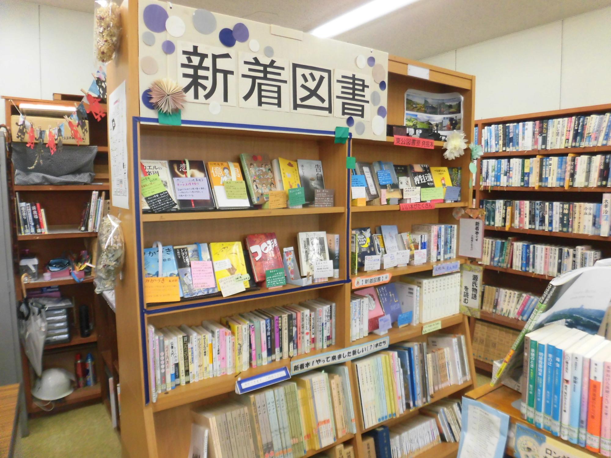 図書館の一角にある「新着図書」と書かれた棚に、小説やエッセイ、実用書など様々なジャンルの本が平積みや背表紙を見せる形で並べられている本棚の写真