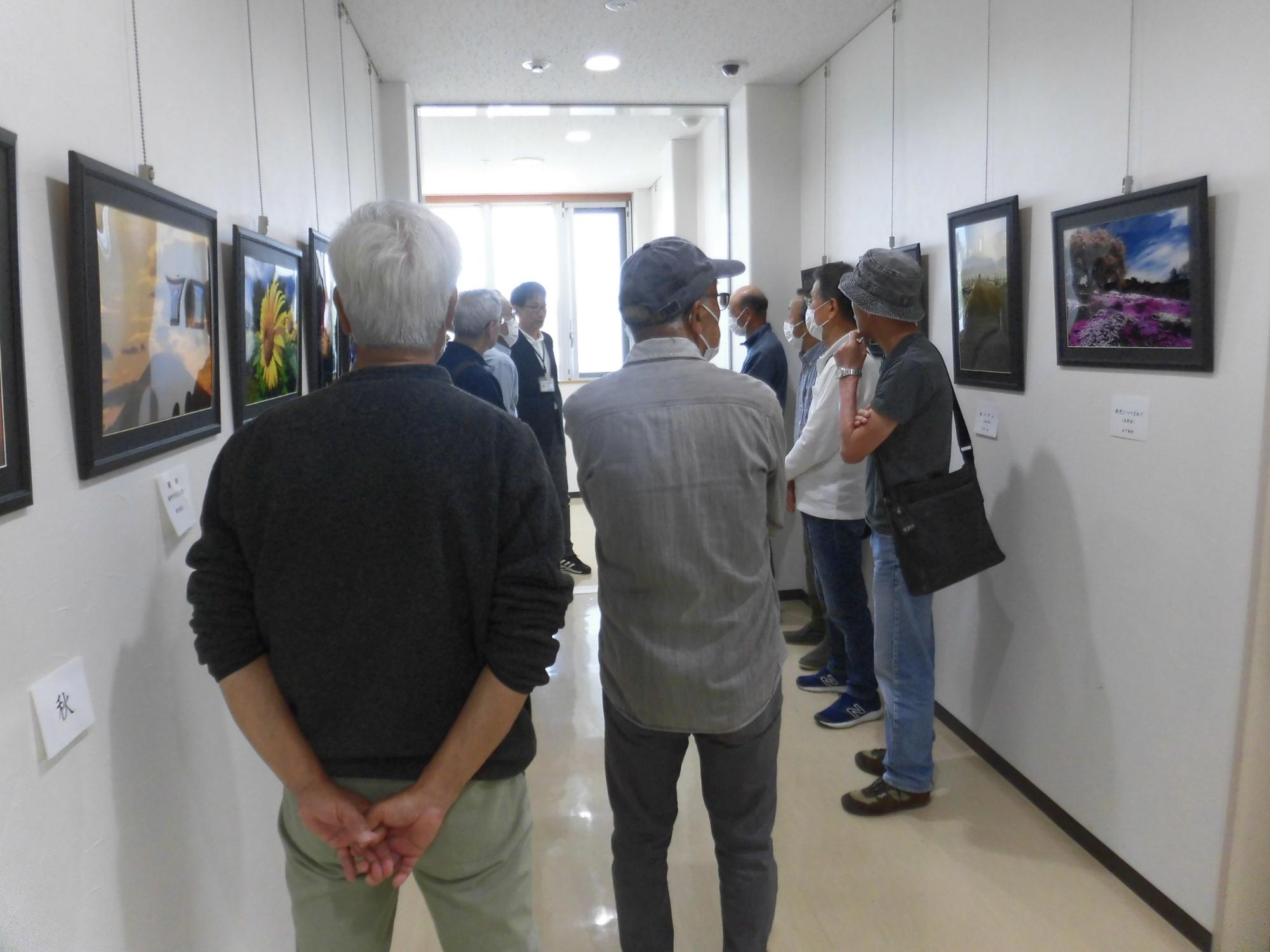 両側の壁に飾られた絵画や写真作品を複数の来場者が鑑賞している様子の写真