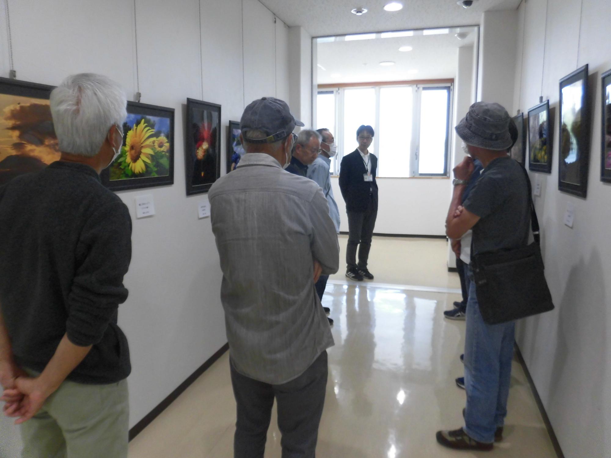 壁に飾られた複数の絵画や写真を、マスクを着用した人々が各自で鑑賞している様子の写真