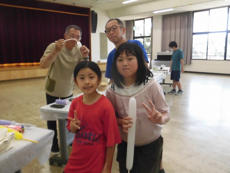 風船で作られた犬のような白い棒状のバルーンを持った子供たちが楽しげにポーズをとっている様子を写した写真