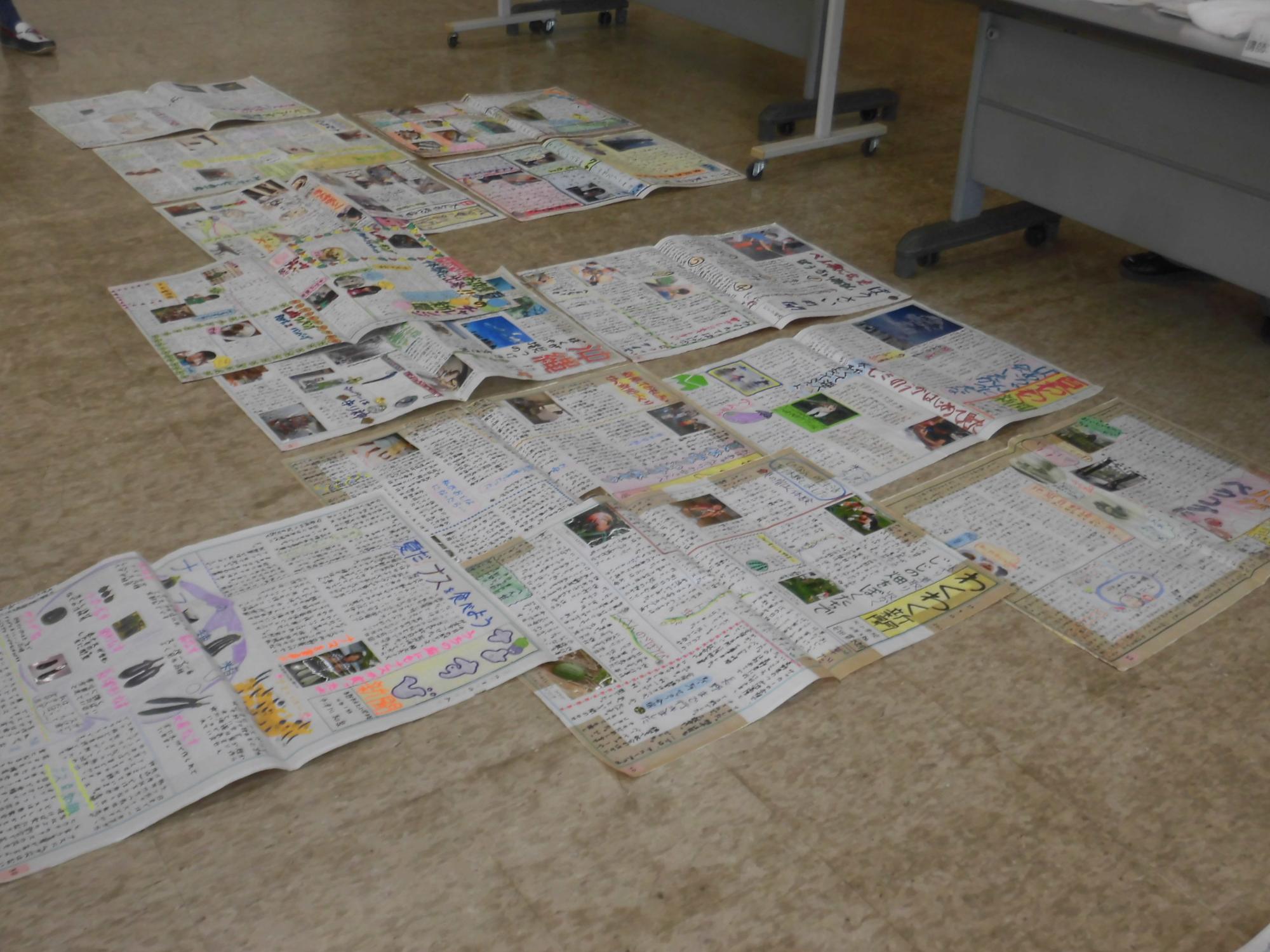 床に広げられた複数の模造紙に、様々な写真やイラスト、手書きの文字がカラフルに書き込まれた、家族新聞の作品を写した写真